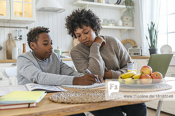 Boy doing homework with mother sitting on table at home