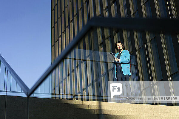 Smiling businesswoman standing near building seen through glass railing