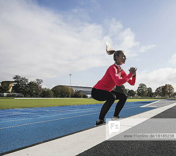 Sportswoman with wireless headphones doing jumping exercise on track