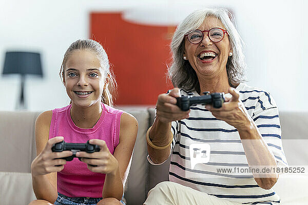 Happy grandmother and granddaughter playing video game with joysticks at home