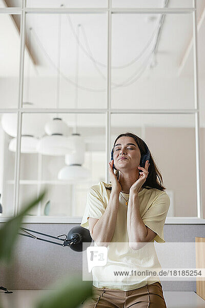 Businesswoman listening to music through wireless headphones in office