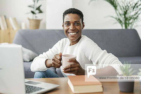 Portrait of smiling woman holding cup of coffee in loving room at home