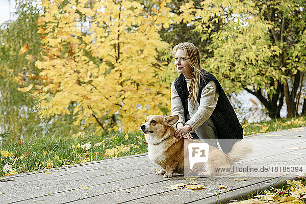 Smiling woman and cute dog on footpath in autumn park