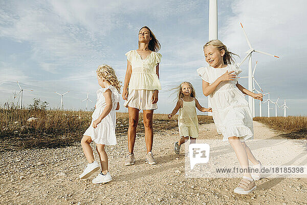Frau spielt an sonnigem Tag mit Töchtern vor Windkraftanlagen