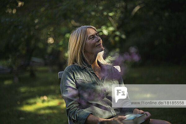 Contemplative mature woman sitting with book in garden