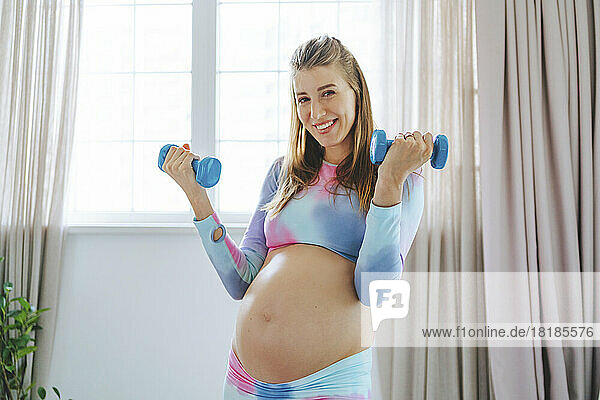 Smiling pregnant woman exercising with dumbbells at home
