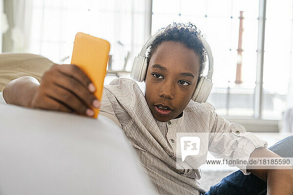 Boy using mobile phone wearing headphones listening to music at home