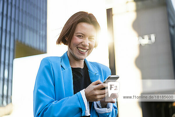 Young businesswoman with smart phone laughing on sunny day