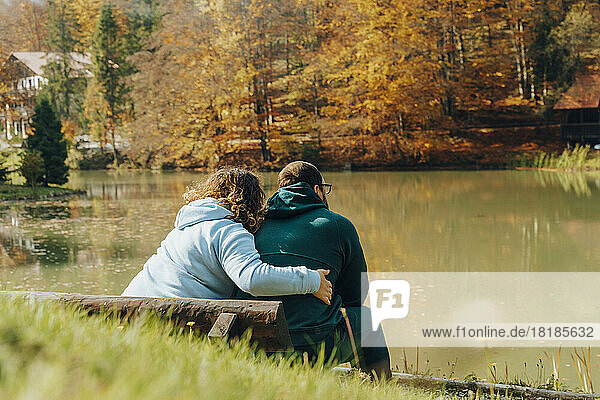 Frau umarmt Mann  der auf Bank am See sitzt