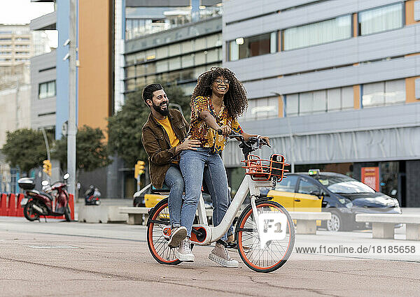 Happy boyfriend enjoying with girlfriend riding bicycle at footpath