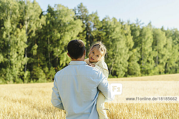 Father carrying daughter in field on sunny day