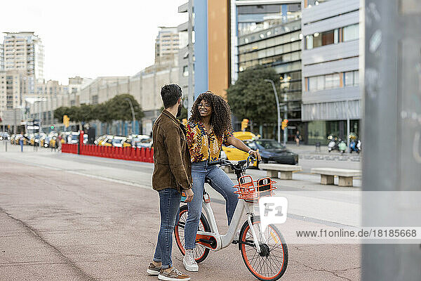 Young man with girlfriend sitting on bicycle at footpath