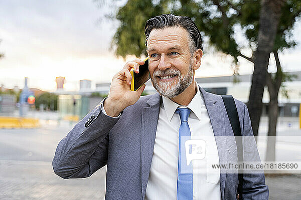 Smiling mature businessman talking on smart phone at street