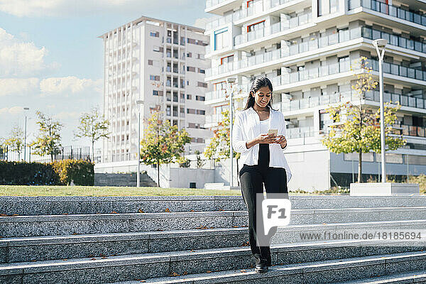 Young woman using smart phone and walking on steps