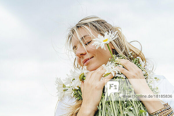 Lächelnde Frau mit geschlossenen Augen  die einen Blumenstrauß hält