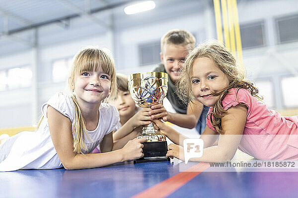 Smiling school students with trophy lying down at school sports court