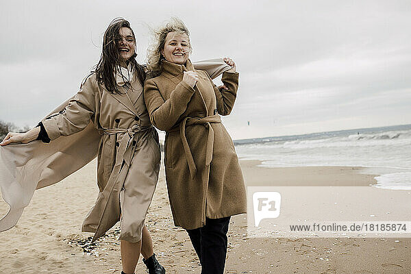 Mutter und Tochter tragen Mäntel und amüsieren sich am Strand