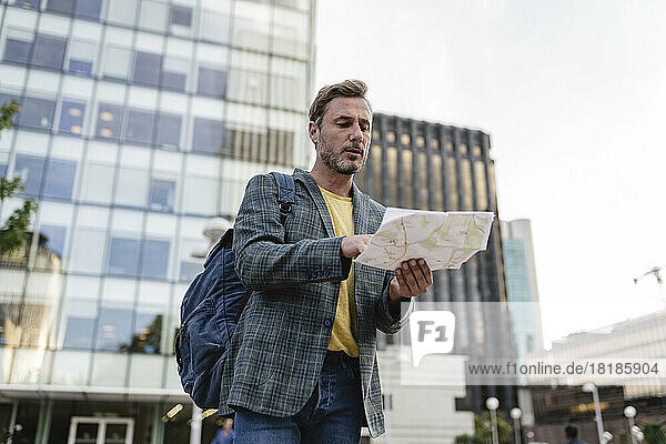 Man with backpack looking at map in city
