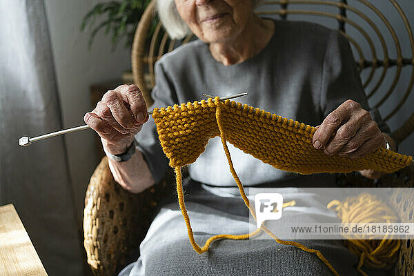 Hands of senior woman knitting scarf at home