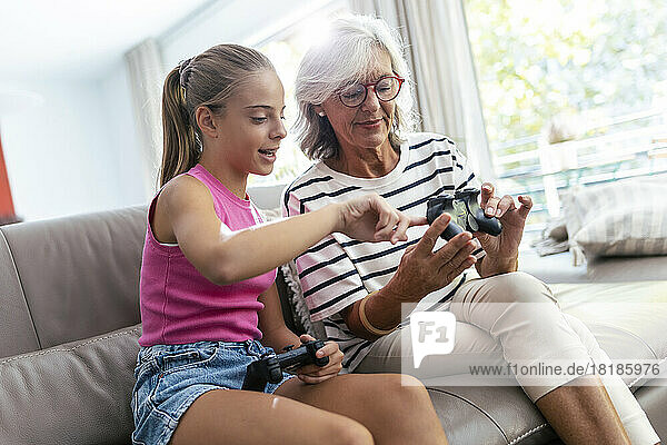 Enkelin spricht mit Großmutter und hält Joystick zu Hause auf dem Sofa