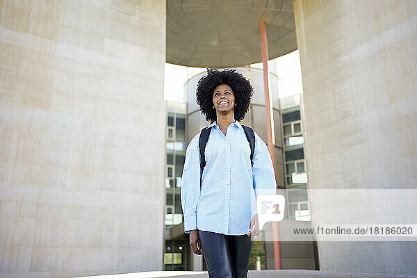 Happy young businesswoman with afro hairstyle walking outside office building