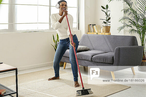 Carefree woman sweeping the floor and listening to music with headphones at home