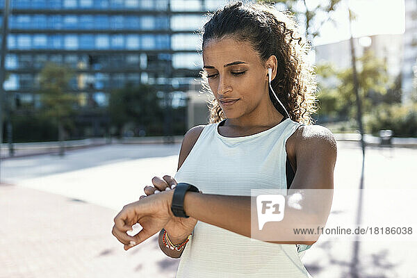 Young woman adjusting smart watch on sunny day