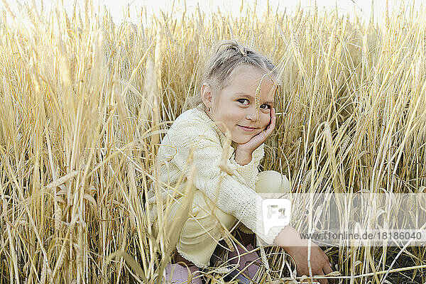 Smiling girl crouching amidst plants in field