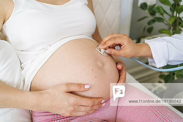 Doctor with stethoscope examining pregnant woman at home