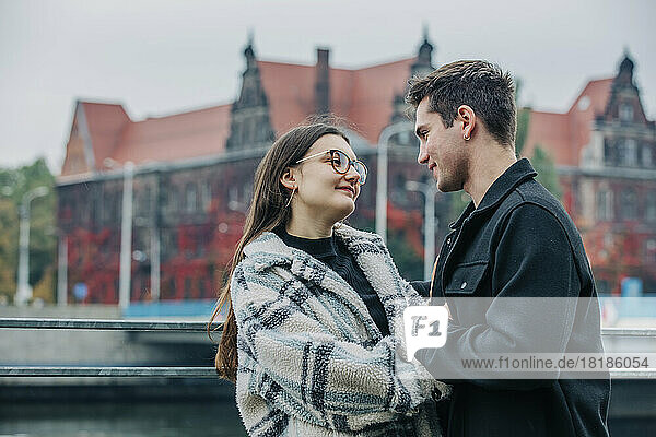 Smiling young couple looking at each other near railing in city