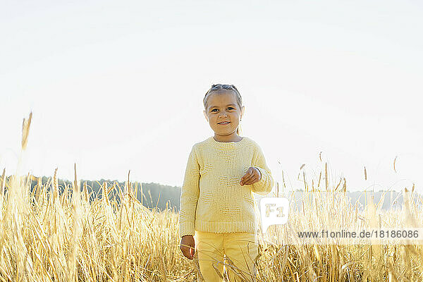 Happy cute girl standing amidst crops at field in front of clear sky