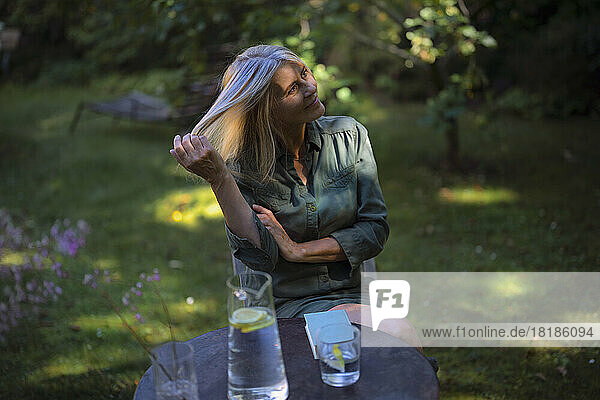 Reife Frau mit der Hand im Haar sitzt im Garten