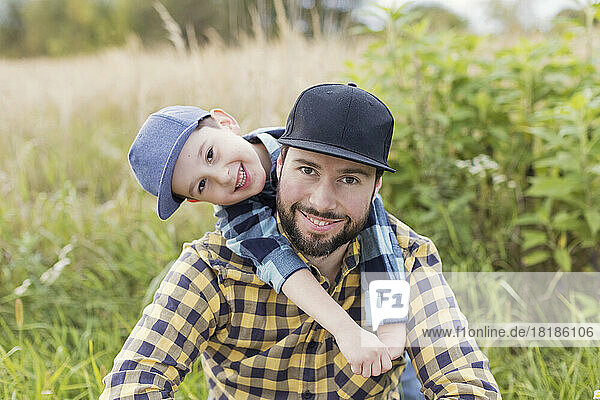 Boy embracing father from behind in meadow