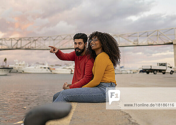 Young man gesturing with woman sitting on promenade at sunset