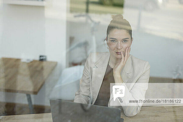 Businesswoman with laptop on table in office seen through glass