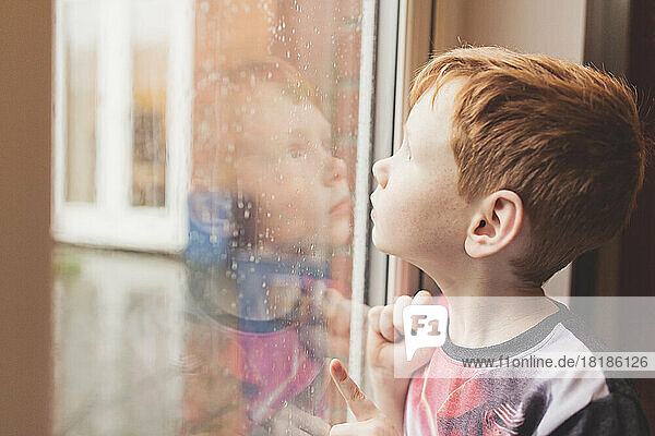 Junge schaut auf den Regen auf der Fensterscheibe