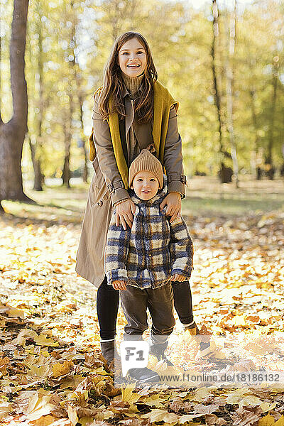 Happy mother and son standing on autumn leaves in park