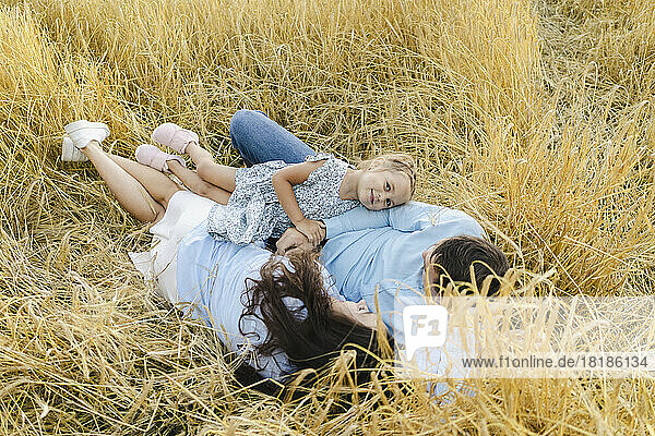 Smiling girl relaxing with father and mother amidst crops in field