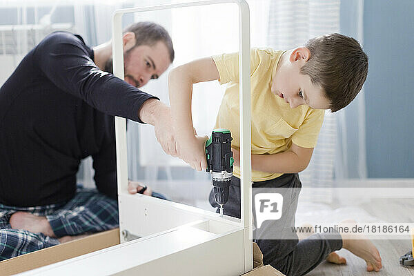 Boy using power screwdriver on table by father at home