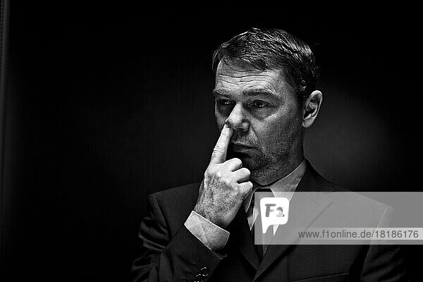 Mature man putting finger in nose against black background