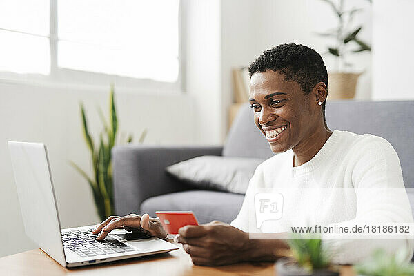 Happy woman holding credit card and using laptop at home