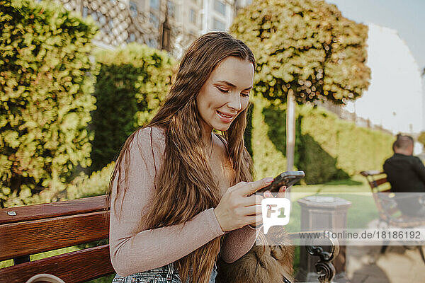 Happy woman using smart phone on bench in park