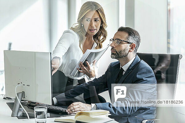 Businesswoman explaining colleague over computer in office