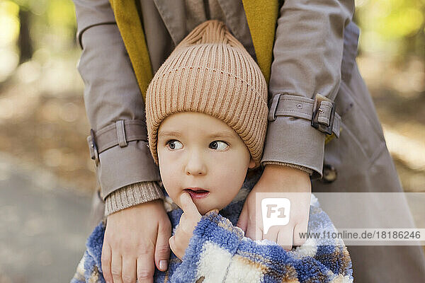 Cute boy wearing knit hat standing with mother in park