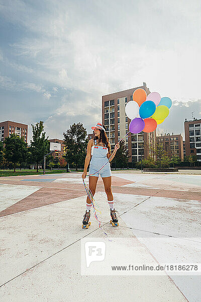 Junge Frau trägt Rollschuhe und hält bunte Luftballons auf dem Sportplatz