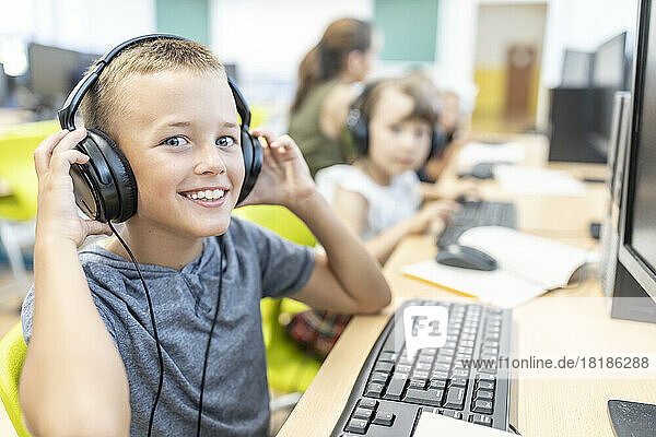 Smiling boy wearing wired headphones in computer class at school
