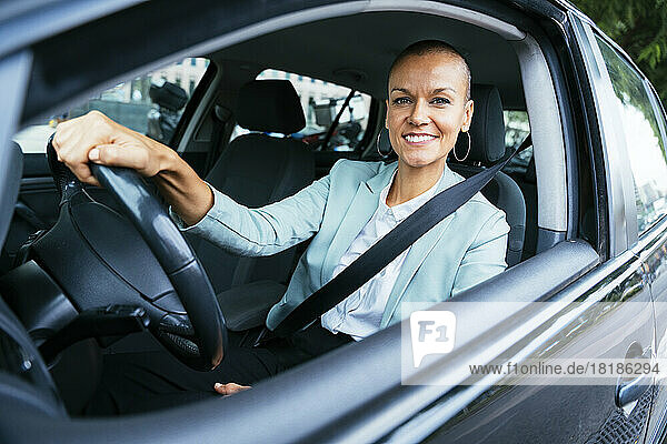 Lächelnde Geschäftsfrau mit Lenkrad im Auto sitzend