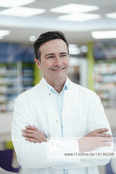 Happy pharmacist with arms crossed in pharmacy