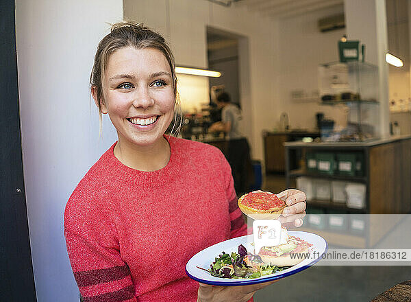 Happy businesswoman with plate of food sitting in cafe