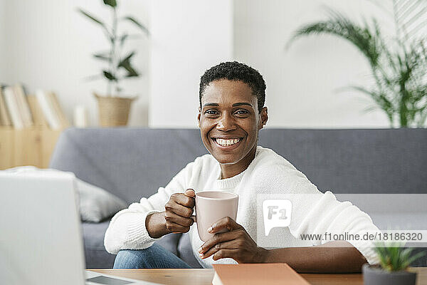 Portrait of smiling woman holding cup of coffee in loving room at home